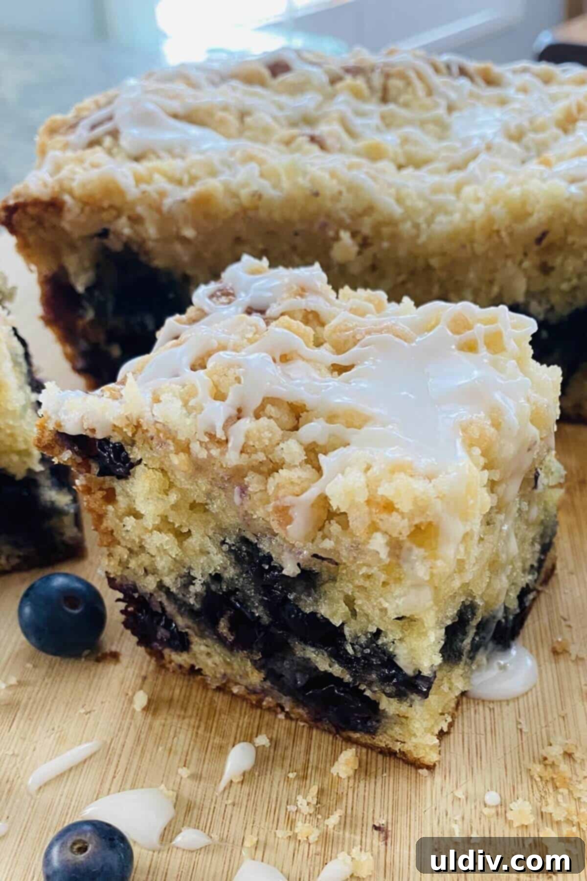 A beautiful slice of blueberry muffin cake, showing its moist interior, fresh blueberries, and crumble topping, with a delicate icing drizzle.