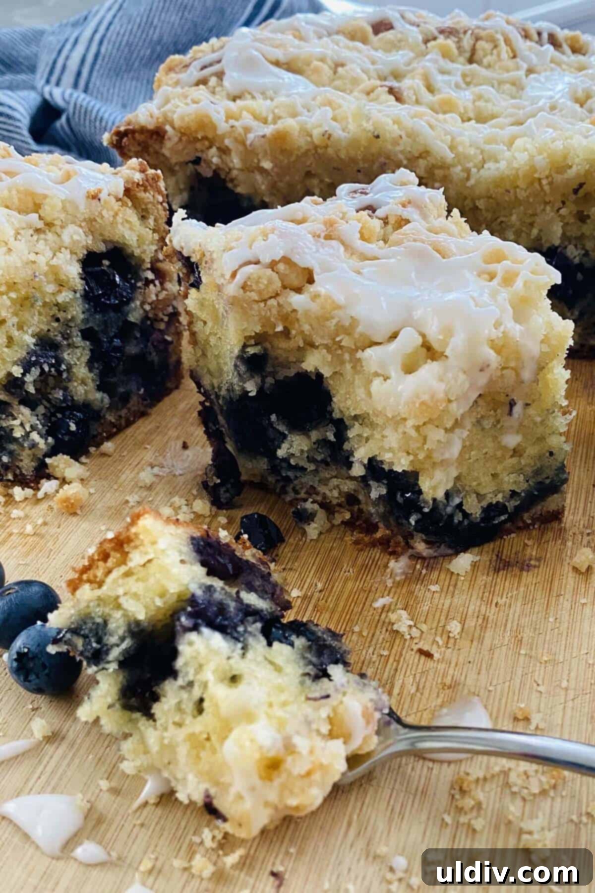 A close-up shot of a bite of blueberry cake on a fork, highlighting the moist texture and juicy blueberries.