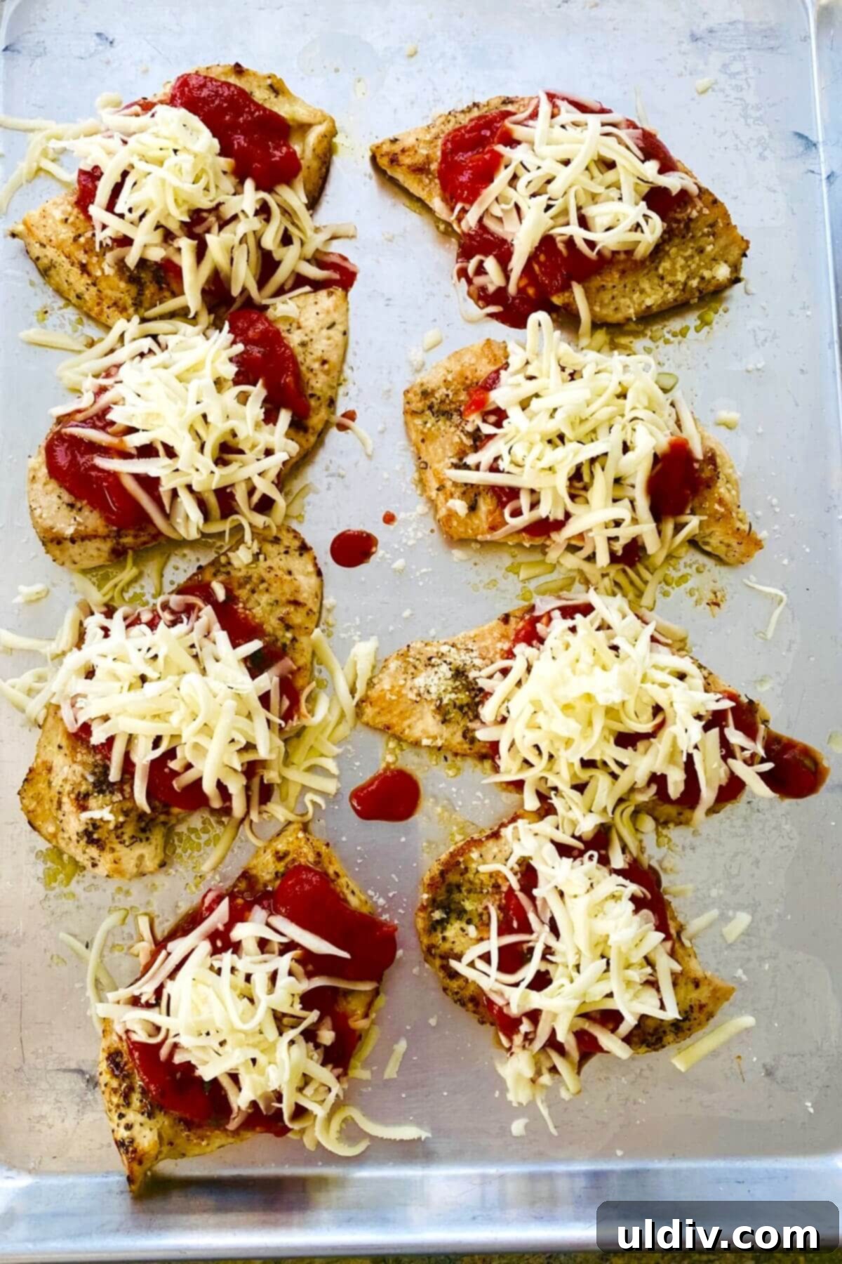 Chicken parmesan topped with cheese and marinara, ready to be baked.