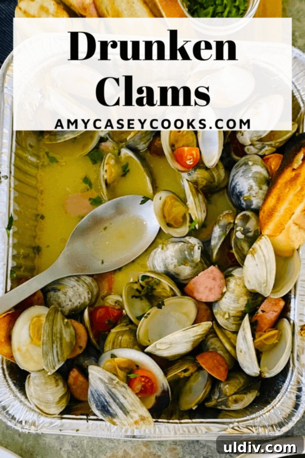 Close-up of clams and sausage in a foil pan with a serving spoon, highlighting the rich broth.