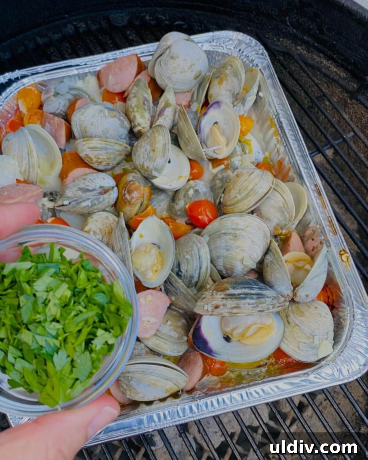 Fresh chopped herbs being sprinkled over cooked drunken clams and sausage.