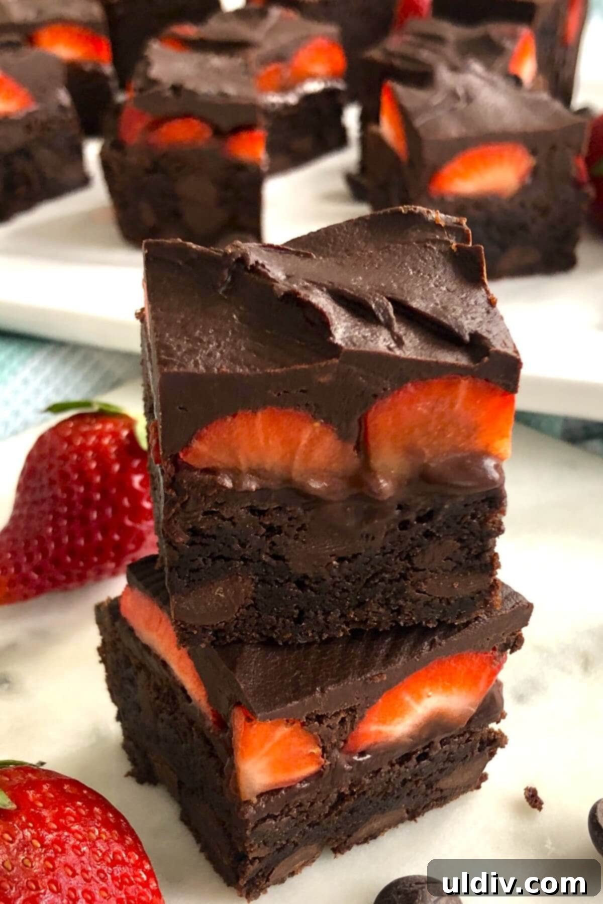 Fudgy Chocolate-Dipped Brownies with Fresh Strawberries 2 A stack of three fudgy chocolate strawberry brownies on a white marble board, showcasing their layers of brownie, fresh strawberries, and glossy ganache.
