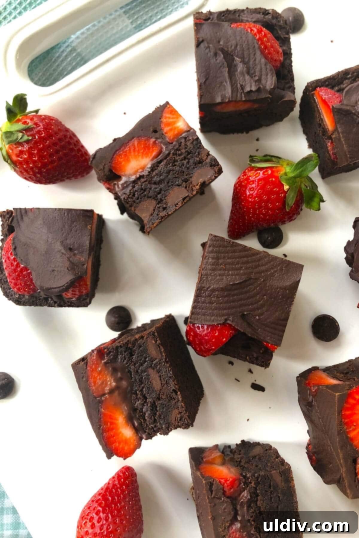 Ultra-Fudgy Chocolate Strawberry Brownie Bliss 3 A white plate featuring perfectly cut fudgy brownies topped with fresh strawberries and a glistening layer of chocolate ganache.