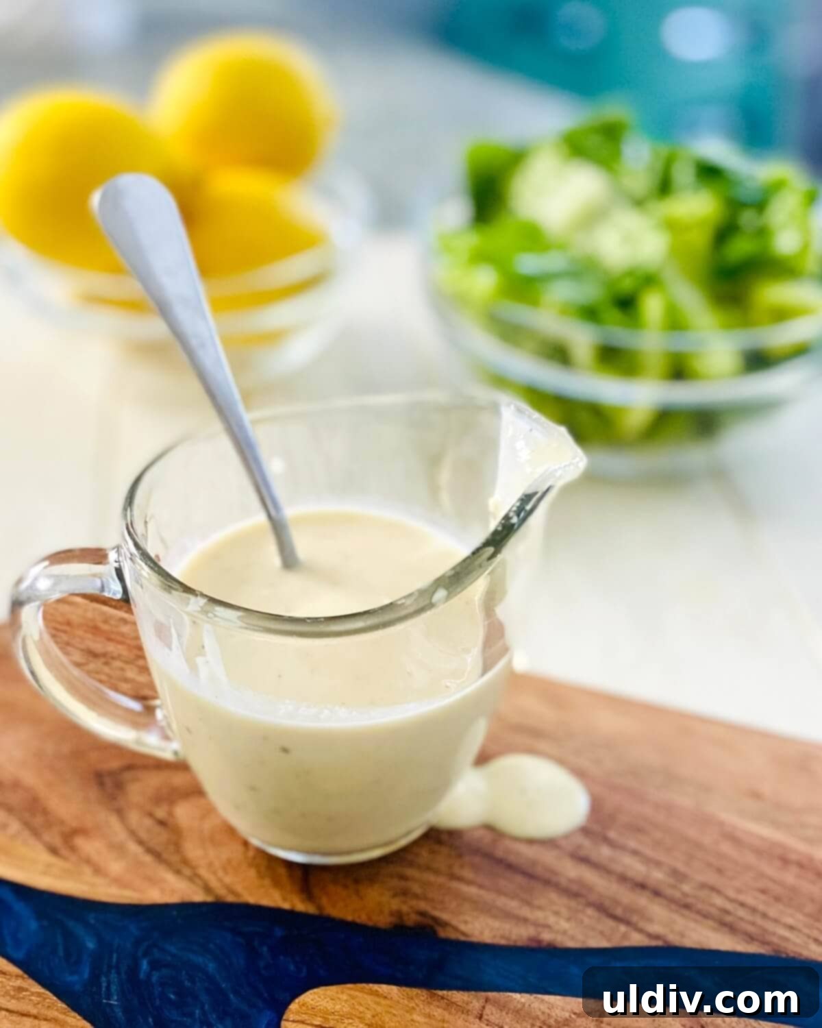 Anchovy-Free Homemade Caesar Dressing 10 A glass pitcher of dressing, bowl of lemons and a bowl of lettuce.