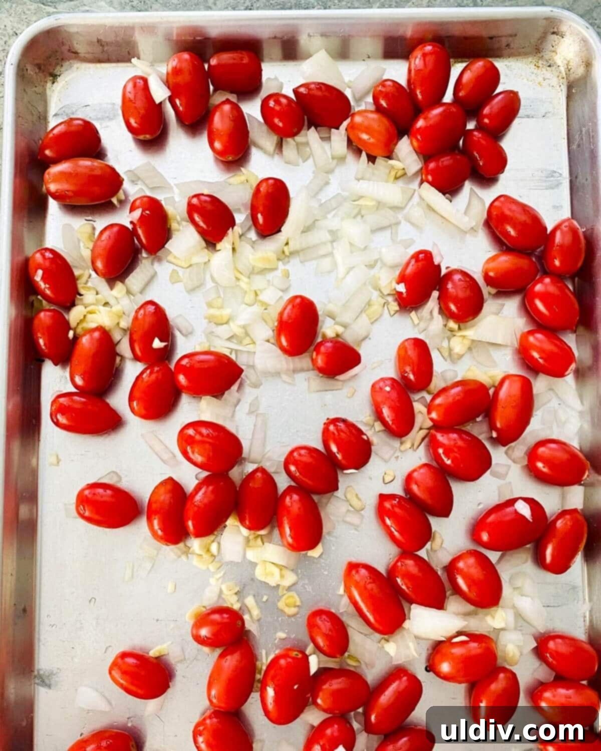 Sweet Oven Roasted Cherry Tomato Pasta 5 Cherry tomatoes, chopped onion, and minced garlic spread in a single layer on a large rimmed baking sheet, ready for roasting.
