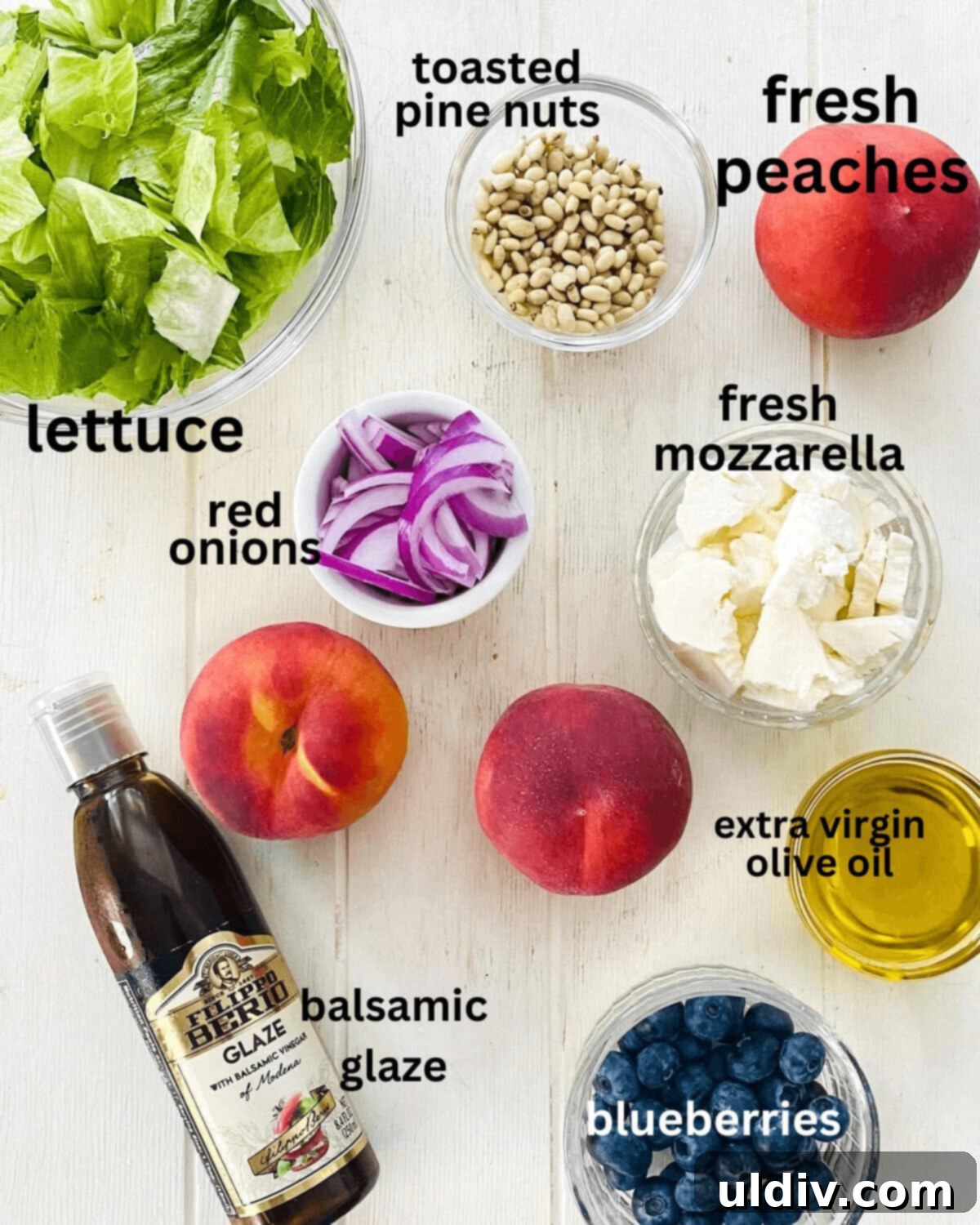 Golden Grille Peach & Creamy Mozzarella Salad 3 Individual ingredients for a grilled peach salad laid out: lettuce, sliced peaches, pine nuts, red onion, mozzarella balls, olive oil, blueberries, and balsamic vinegar.