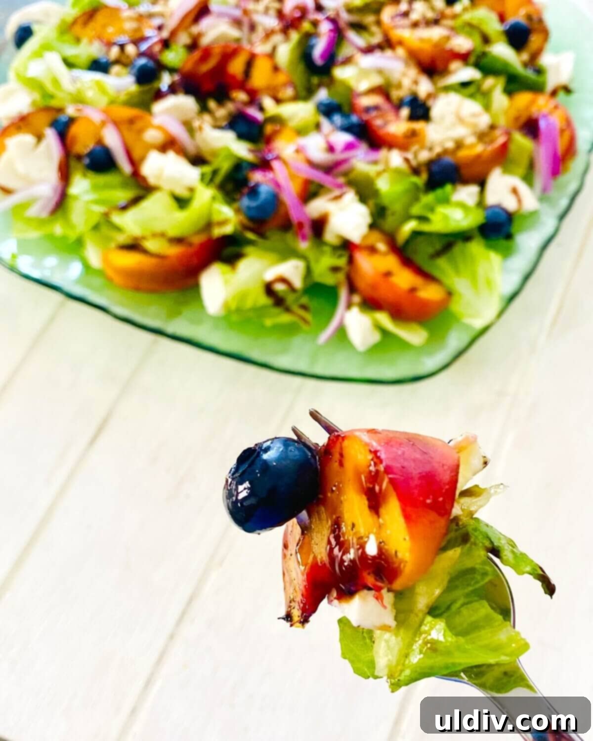Sweet and Savory Grilled Peach Mozzarella Salad 10 a fork with a blueberry, lettuce, grilled peach and red onion.