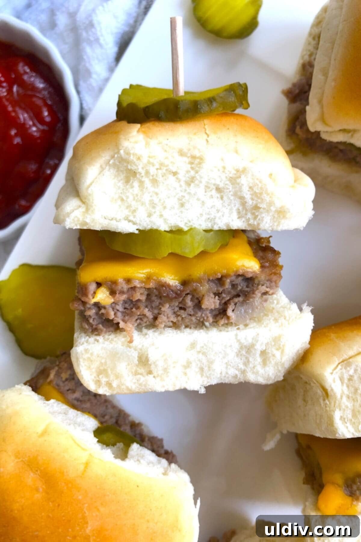 Ultimate Crowd-Pleasing Cheeseburger Sliders 2 A single cheeseburger slider with a dill pickle chip on the side, showcasing the melted cheese and soft bun.