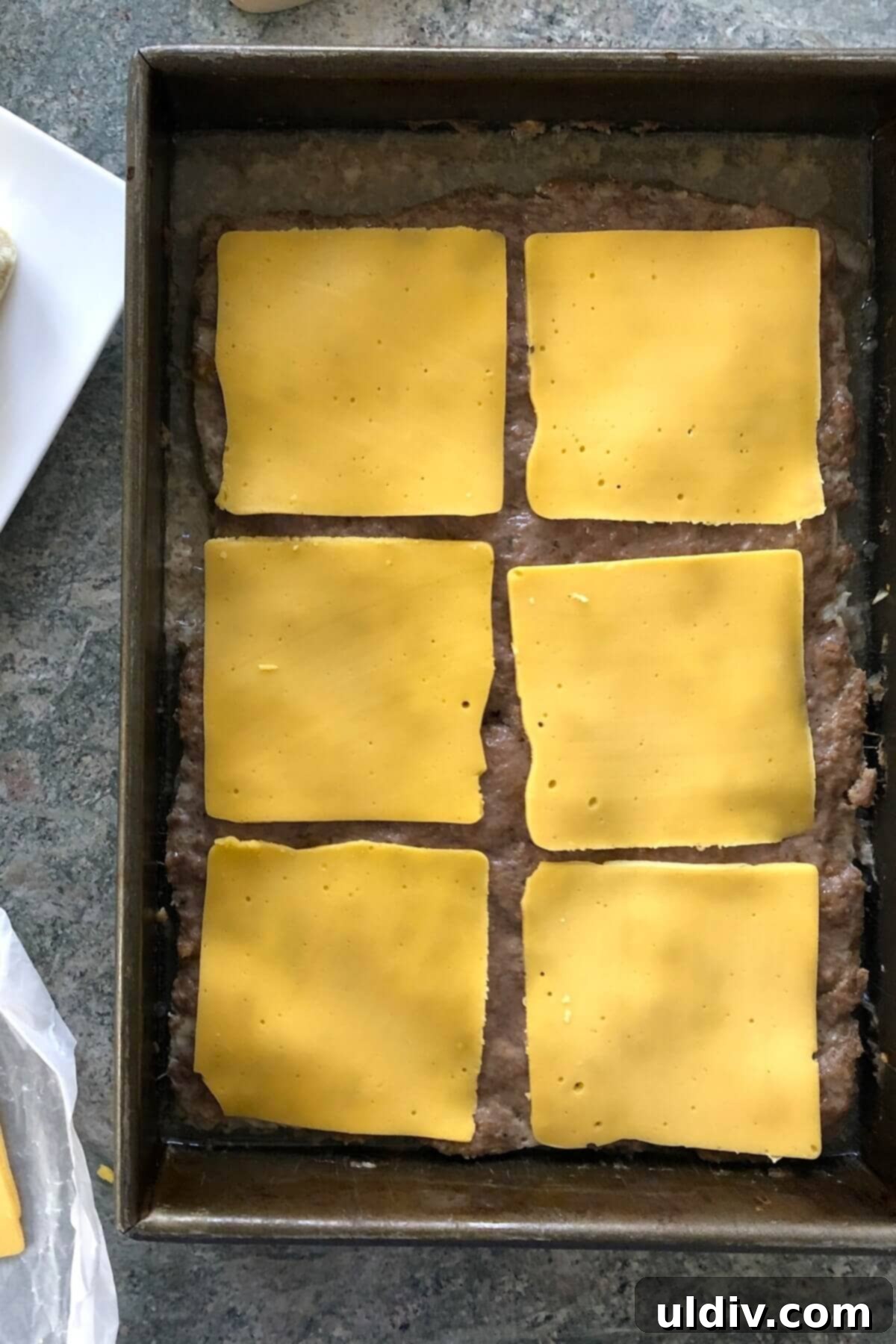 Ultimate Crowd-Pleasing Cheeseburger Sliders 8 A large baked burger patty with American cheese slices on top, just before melting.