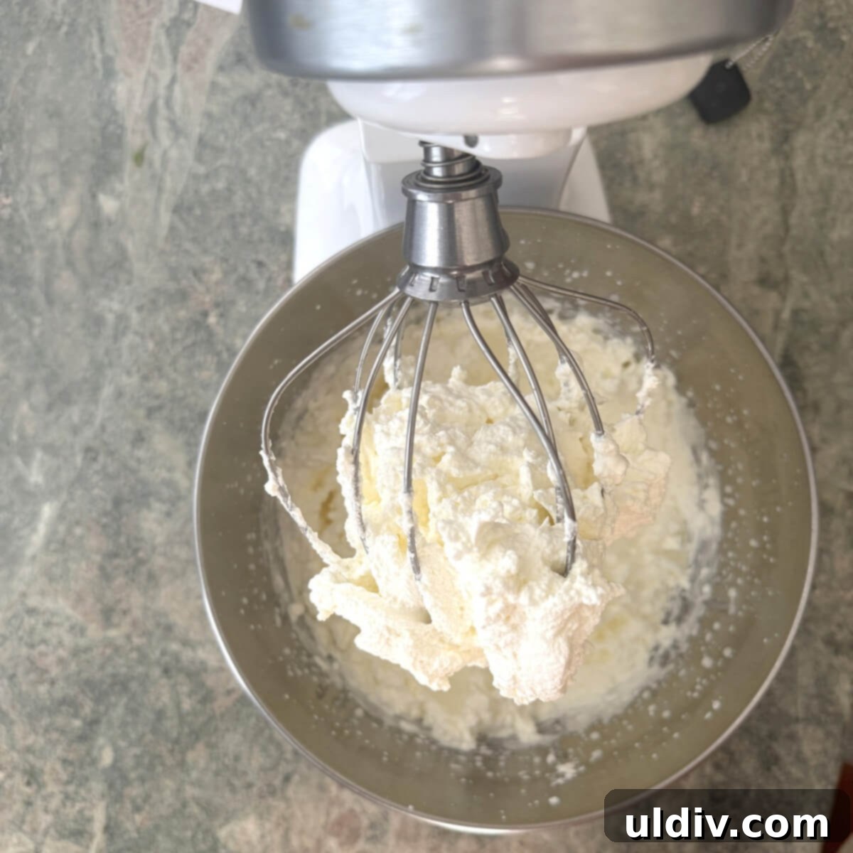 Homemade whipped cream on a beater, showing stiff peaks.