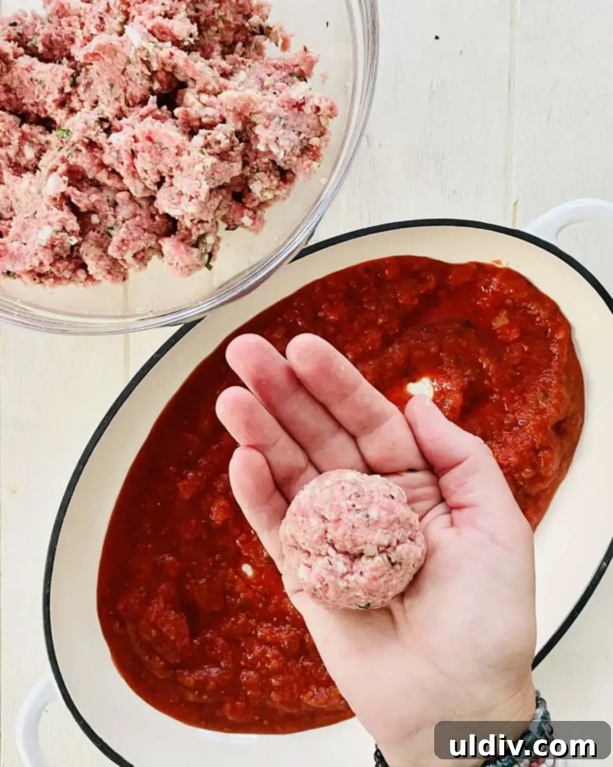A hand gently forming a raw meatball from the prepared mixture, showcasing its consistent texture.