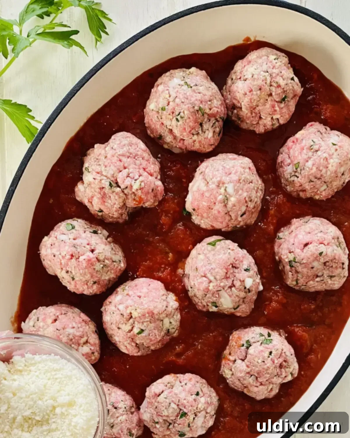 Uncooked Italian meatballs nestled in a bed of vibrant marinara sauce in a baking dish, sprinkled with Parmesan cheese before baking.