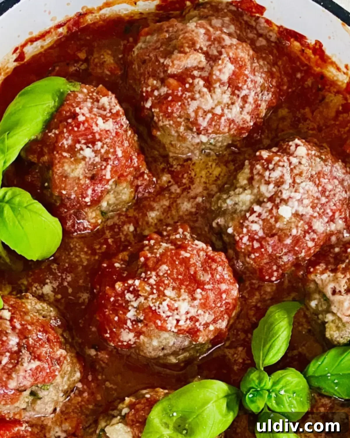 Four hearty meatballs covered in rich marinara sauce, garnished with fresh basil, ready to be enjoyed.