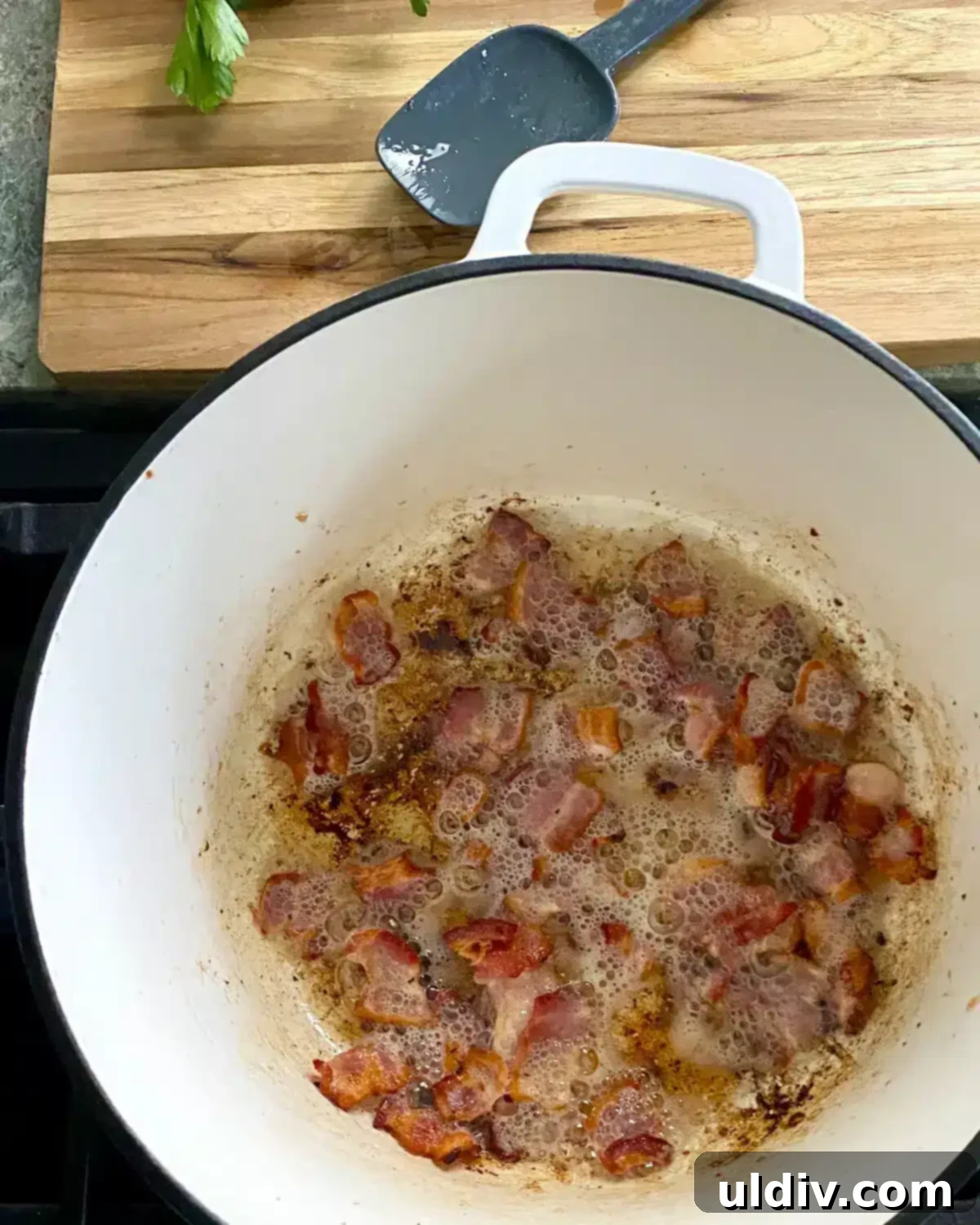 Hearty Pork Tenderloin and Bacon Stew 4 Cooking crispy bacon pieces in a white Dutch oven, ready to be removed.