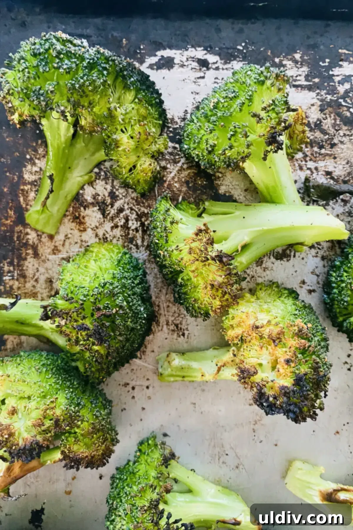 Golden Garlic Roasted Broccoli 12 A close-up view of broiled broccoli on a baking sheet, highlighting its crispy, charred texture.