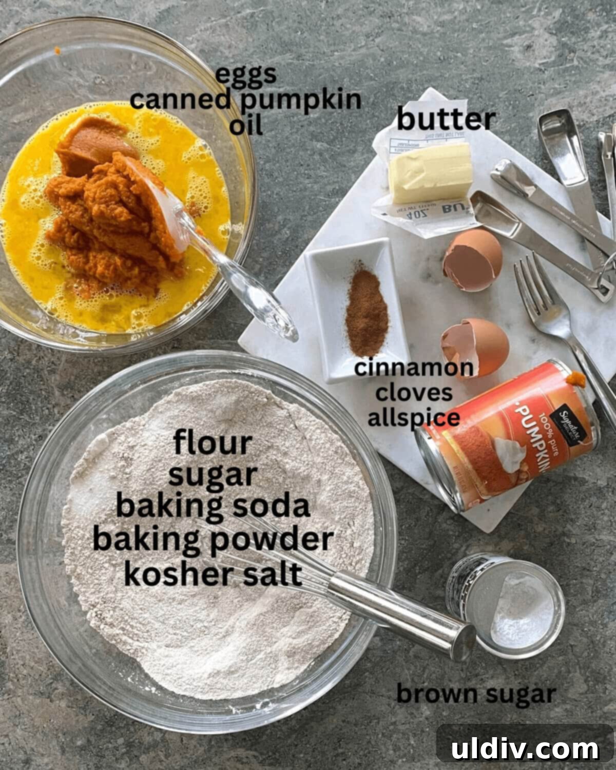 Delicious Mini Pumpkin Loaves 3 A vibrant arrangement of baking ingredients for pumpkin bread, including flour, sugar, eggs, canned pumpkin, cinnamon sticks, butter, cloves, and allspice on a rustic counter.