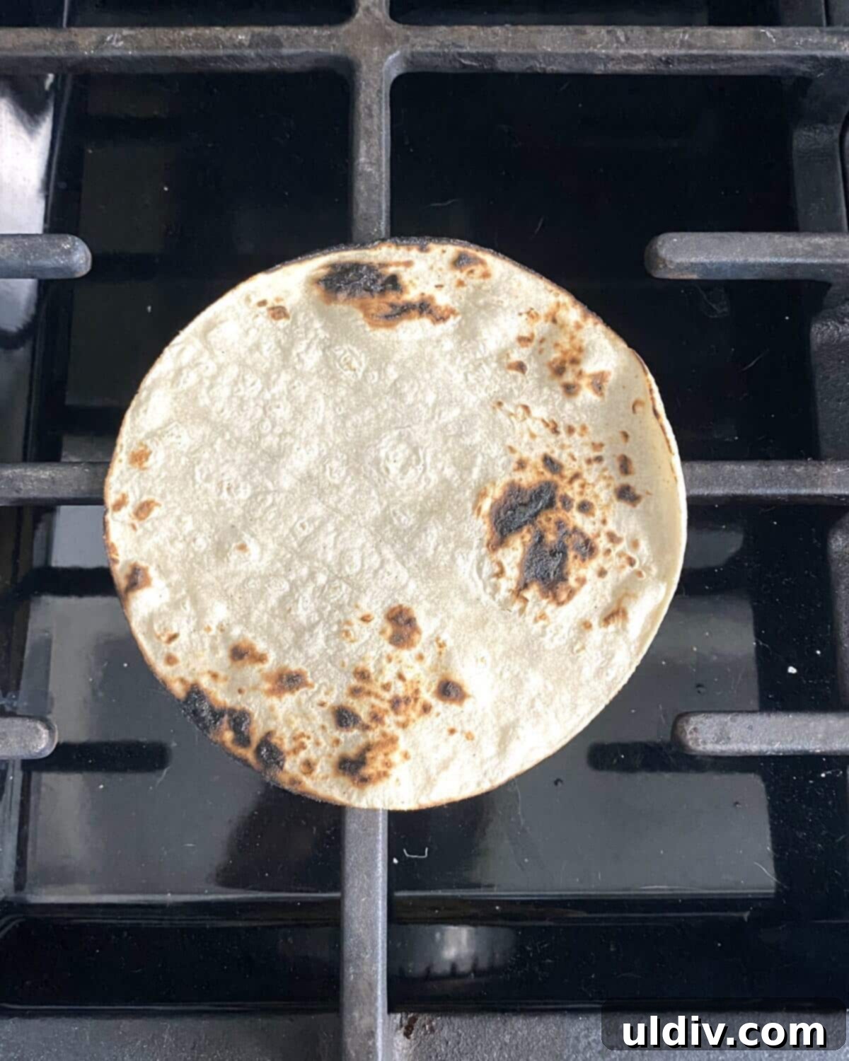 Irish Tacos: The Corned Beef & Cabbage Twist 6 A corn tortilla being charred over a stovetop flame, showing slight browning.