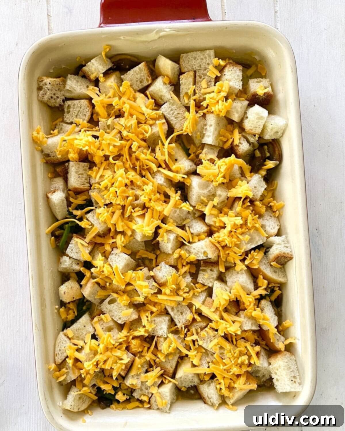 Sausage, Mushroom & Spinach Breakfast Strata 12 The unbaked egg casserole topped with seasoned bread cubes and a sprinkle of cheese, ready for the oven.