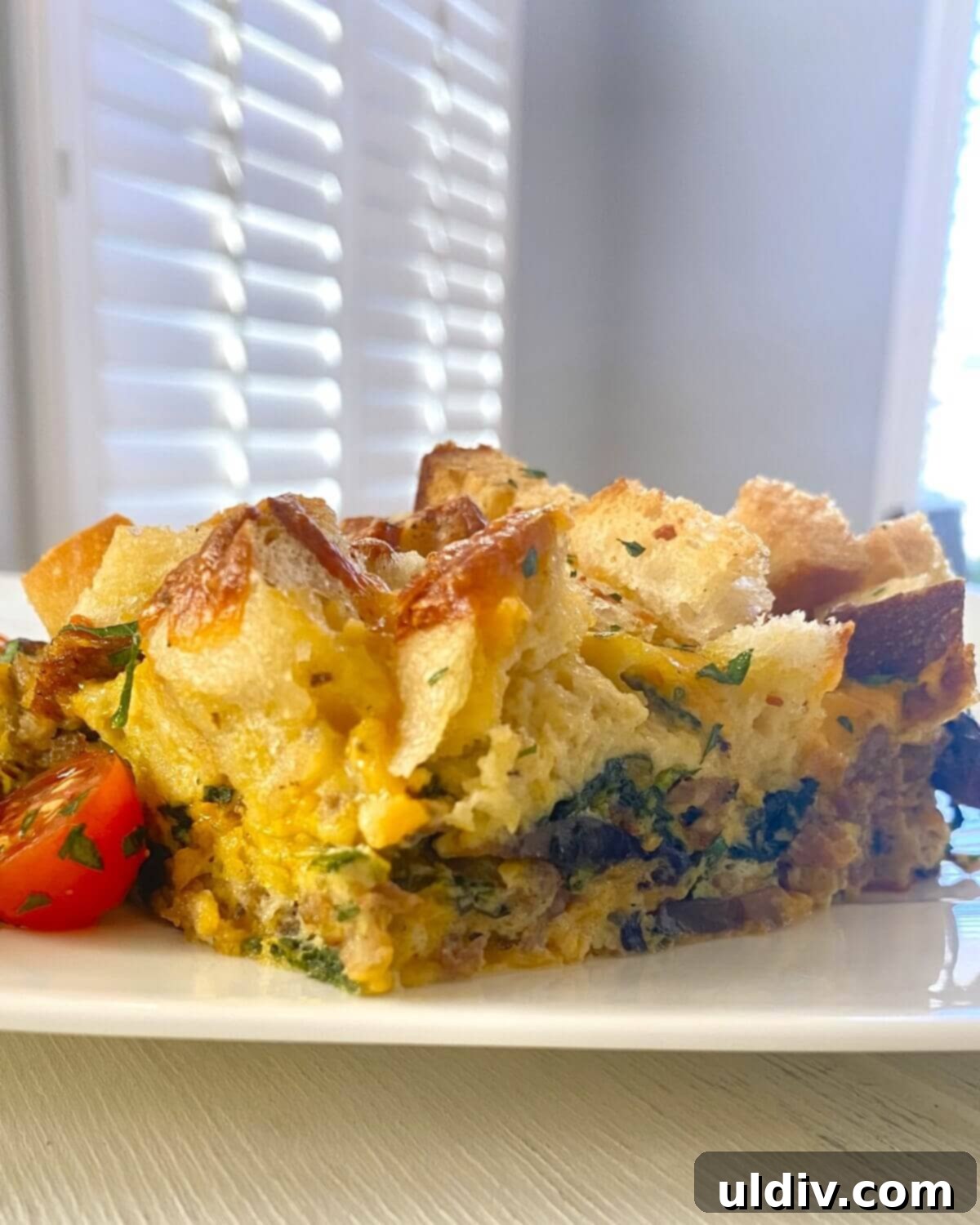Sausage, Mushroom & Spinach Breakfast Strata 14 A perfectly baked slice of egg casserole with golden croutons, accompanied by fresh cherry tomatoes on the side.