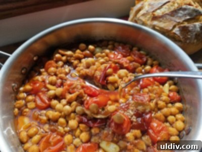 Confit Tandoori Chickpeas: A Fusion of Flavors 6 A close-up of the simmering Confit Tandoori Chickpeas in a pan, showcasing the rich, aromatic oil and tender texture, with spices visibly infused.