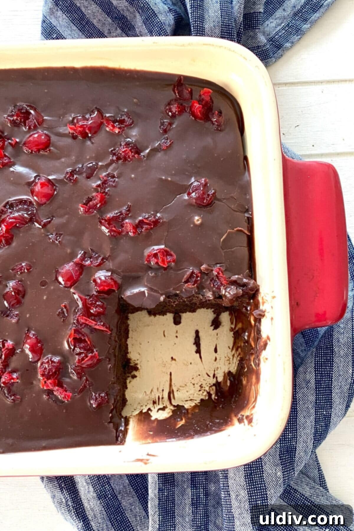 A whole Chocolate Cherry Cake with a slice removed, revealing its moist, cherry-studded interior and thick, fudgy icing.