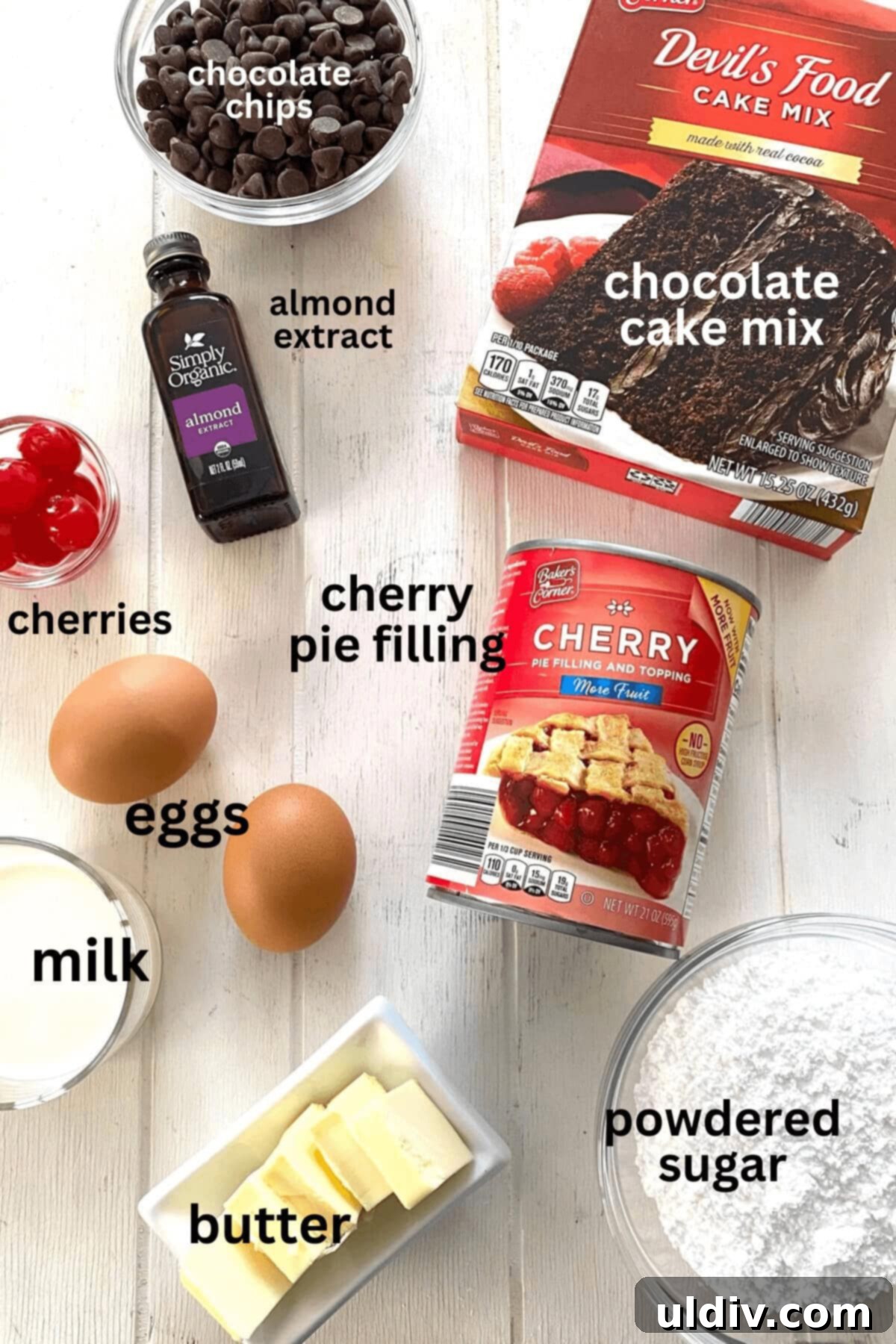 All the essential ingredients neatly laid out for baking the Chocolate Cherry Cake, including cake mix, cherry pie filling, eggs, chocolate chips, butter, milk, and extracts.