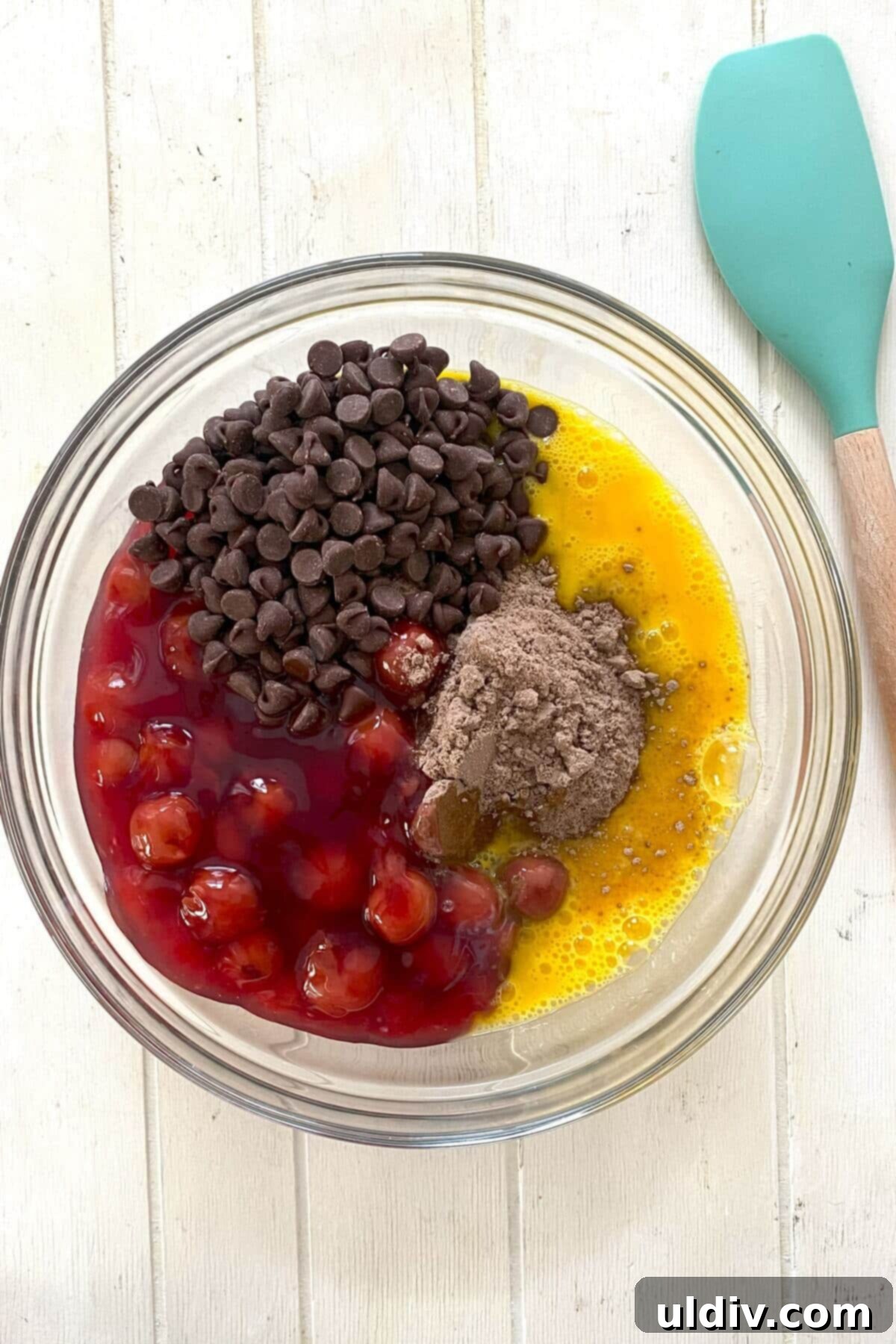 A large mixing bowl containing chocolate cake mix, cherry pie filling, eggs, and chocolate chips, ready to be combined for the cake batter.