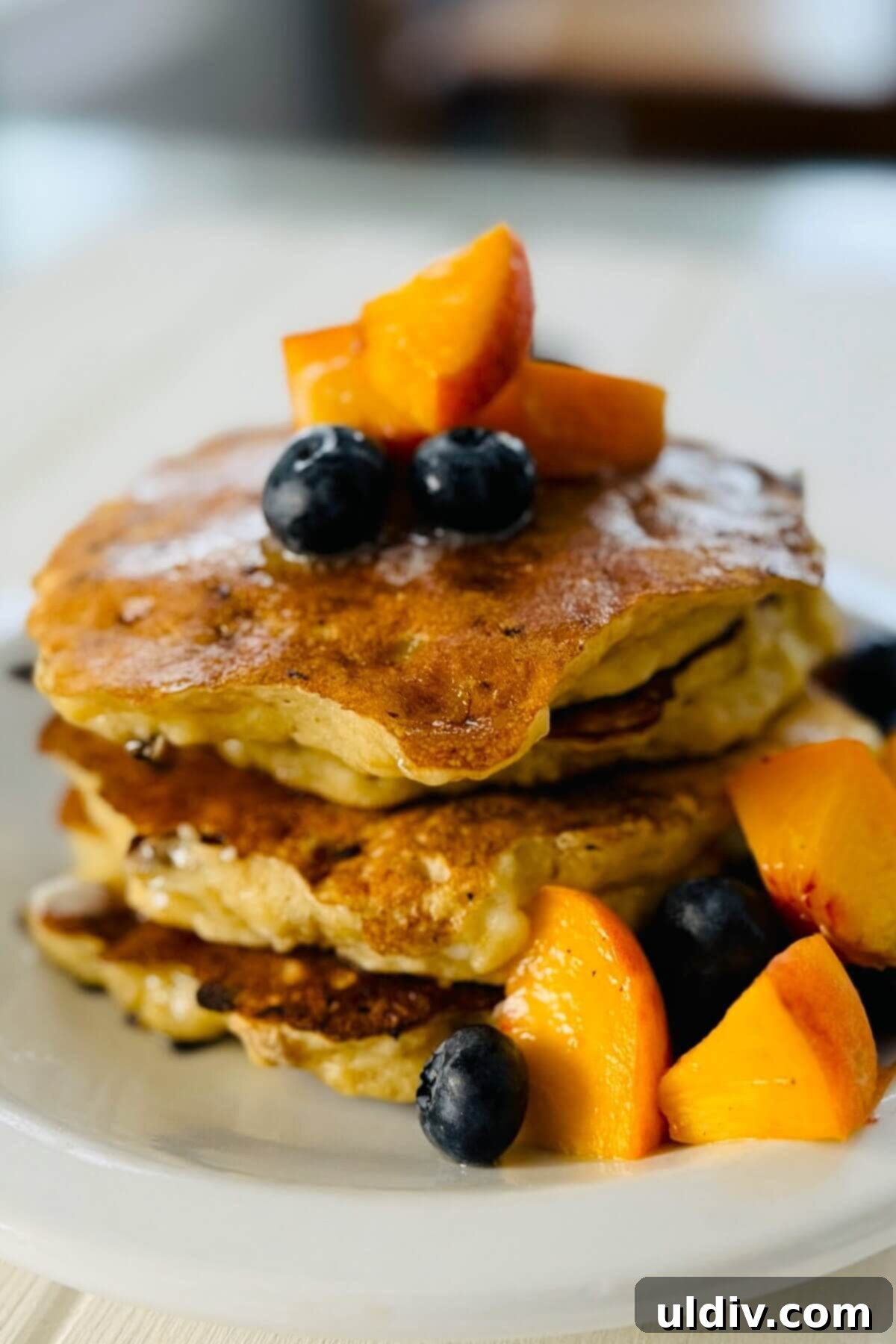 Wholesome Banana Cottage Cheese Protein Pancakes 2 A vibrant stack of three golden-brown protein pancakes topped with sliced peaches and fresh blueberries, ready for a healthy breakfast.