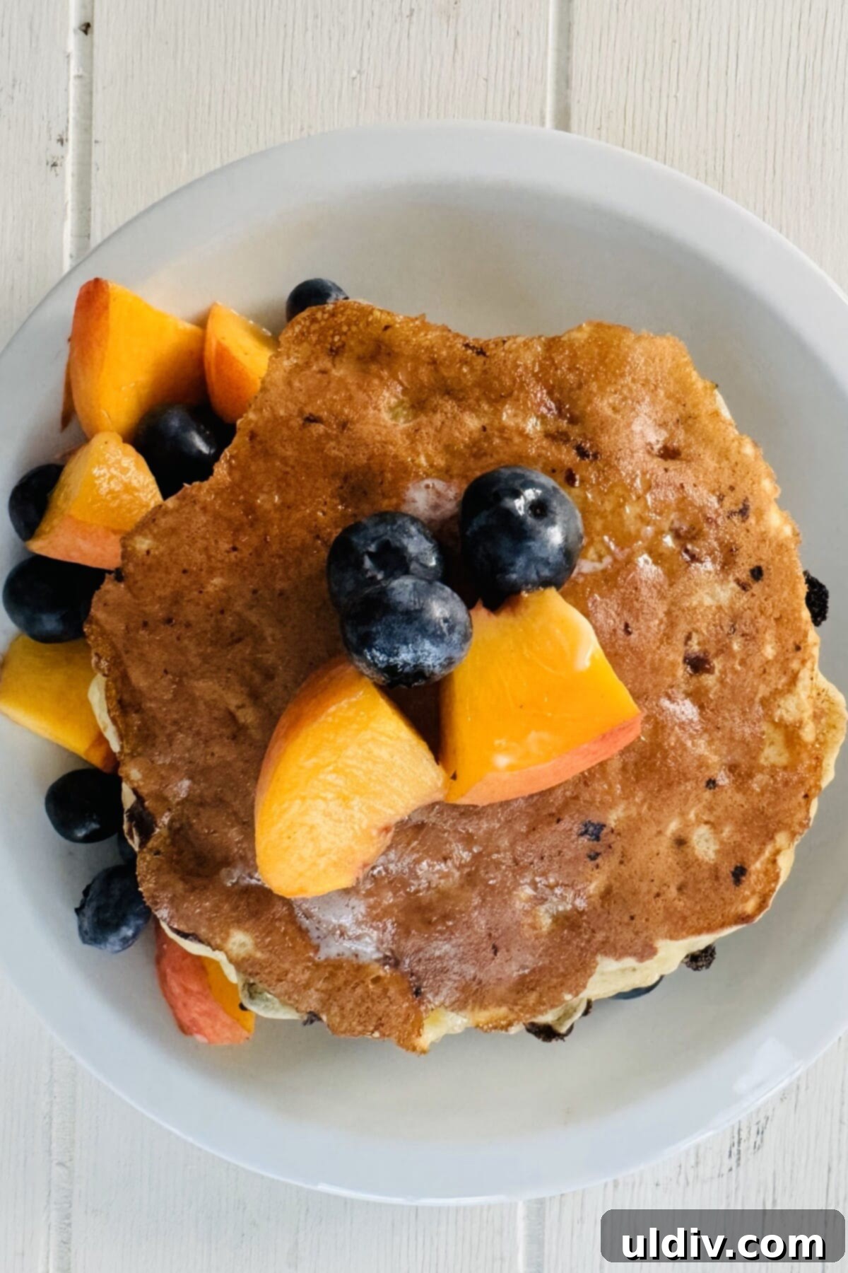 Power-Packed Banana Cottage Cheese Protein Pancakes 13 A single protein pancake on a white plate, beautifully topped with sliced peaches and fresh blueberries.