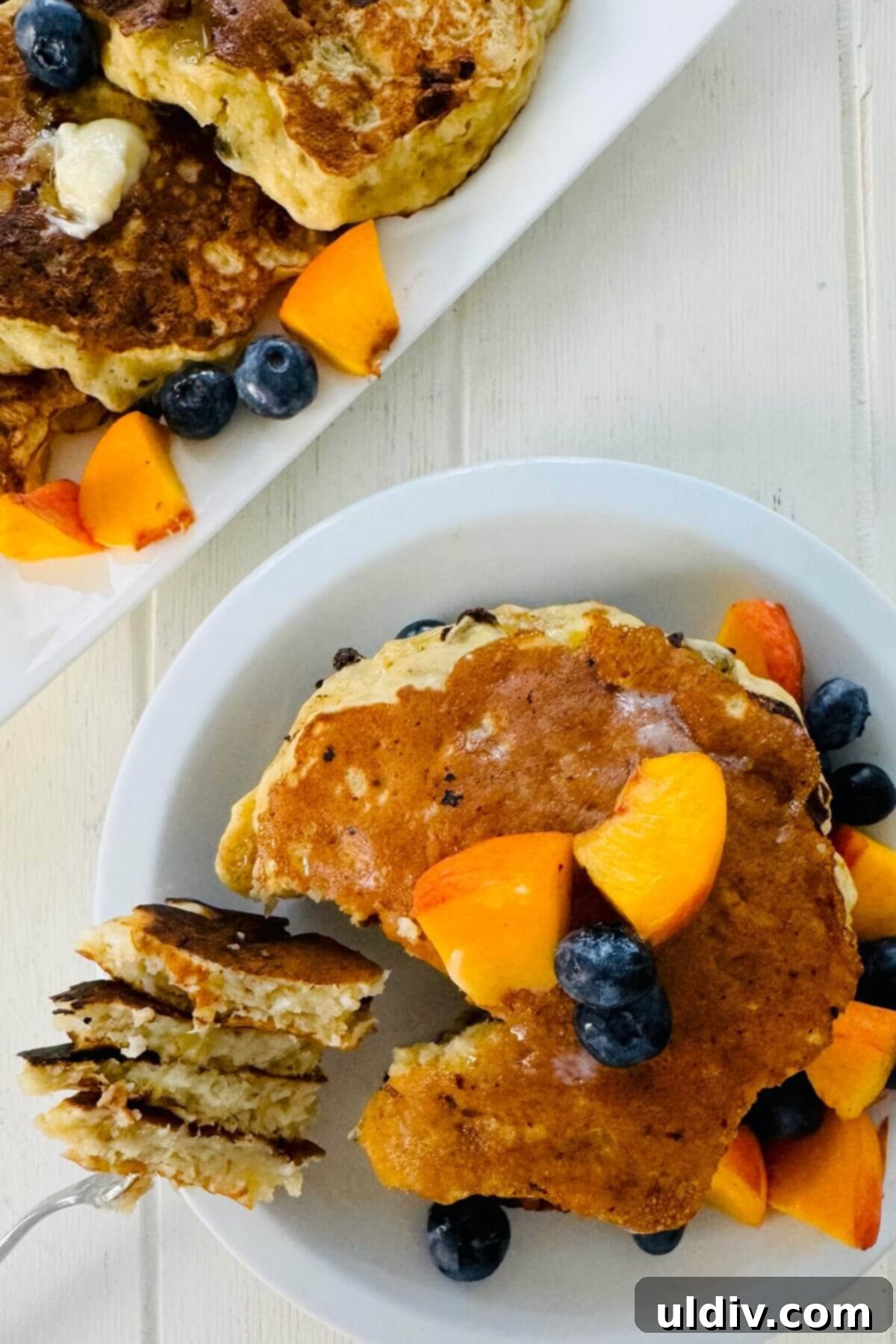 Power-Packed Banana Cottage Cheese Protein Pancakes 3 A close-up of a stack of cottage cheese pancakes with a piece on a fork, showing their light and fluffy texture.