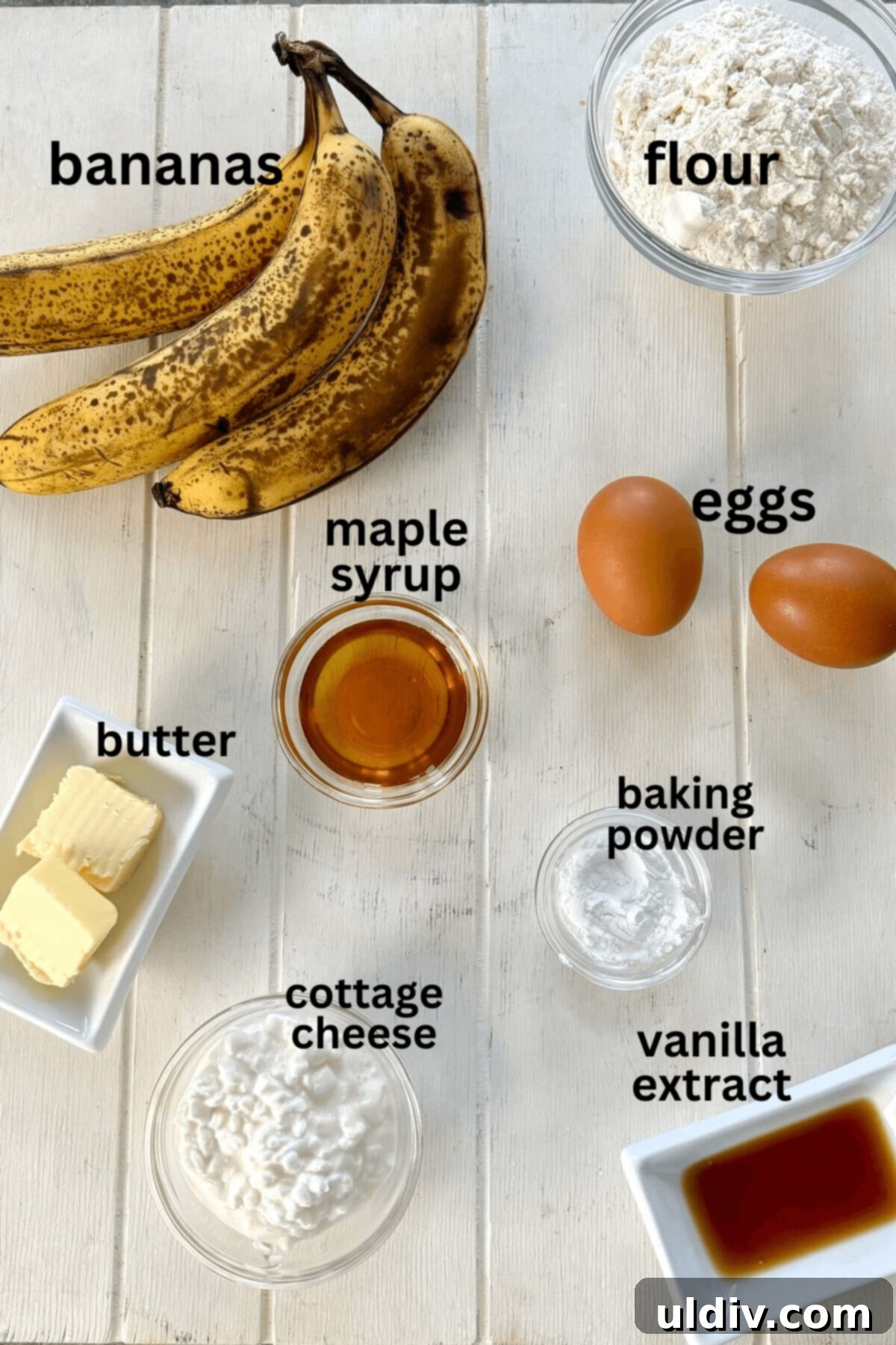 Wholesome Banana Cottage Cheese Protein Pancakes 4 A selection of fresh ingredients including ripe bananas, eggs, maple syrup, butter, vanilla extract, cottage cheese, all-purpose flour, and baking powder arranged neatly.