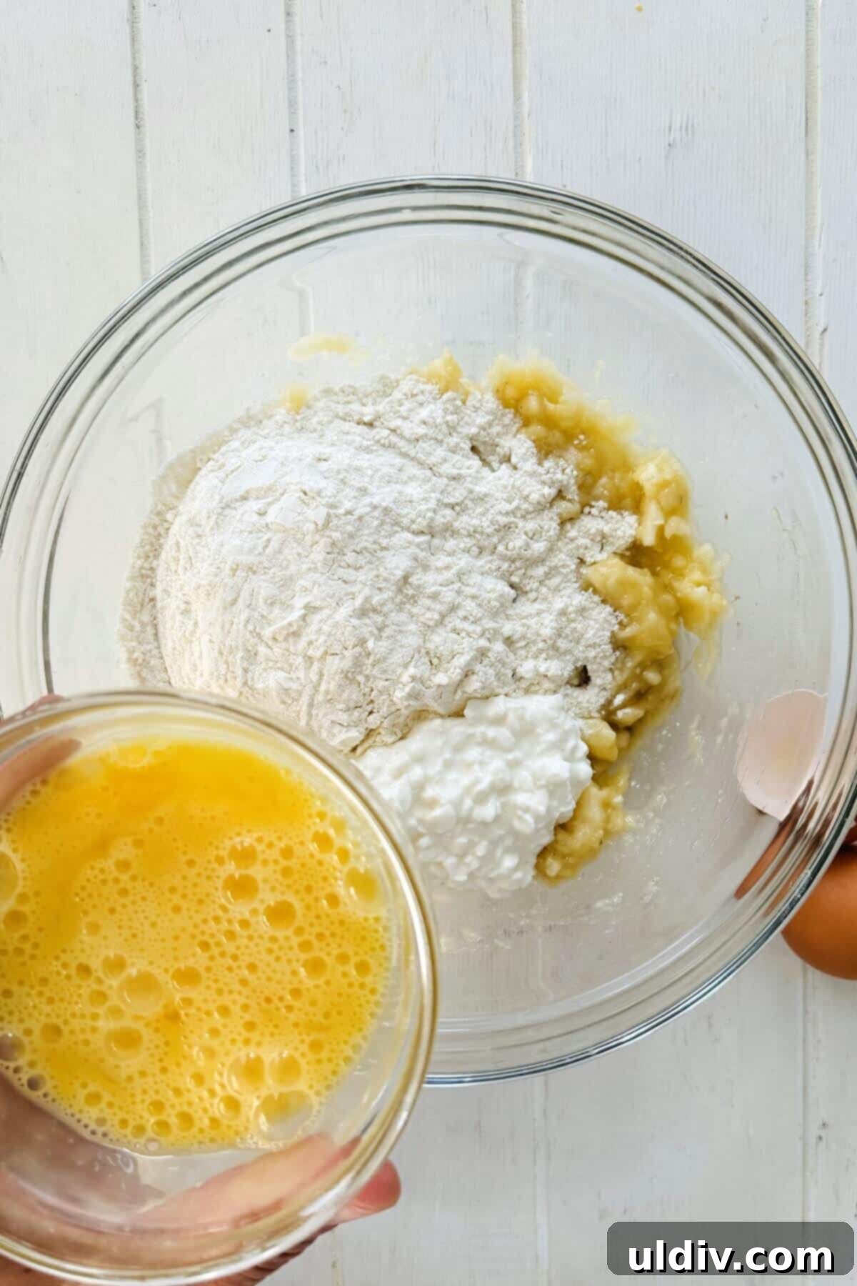 Wholesome Banana Cottage Cheese Protein Pancakes 6 Adding all-purpose flour, cottage cheese, and beaten eggs to mashed bananas in a bowl for pancake batter.
