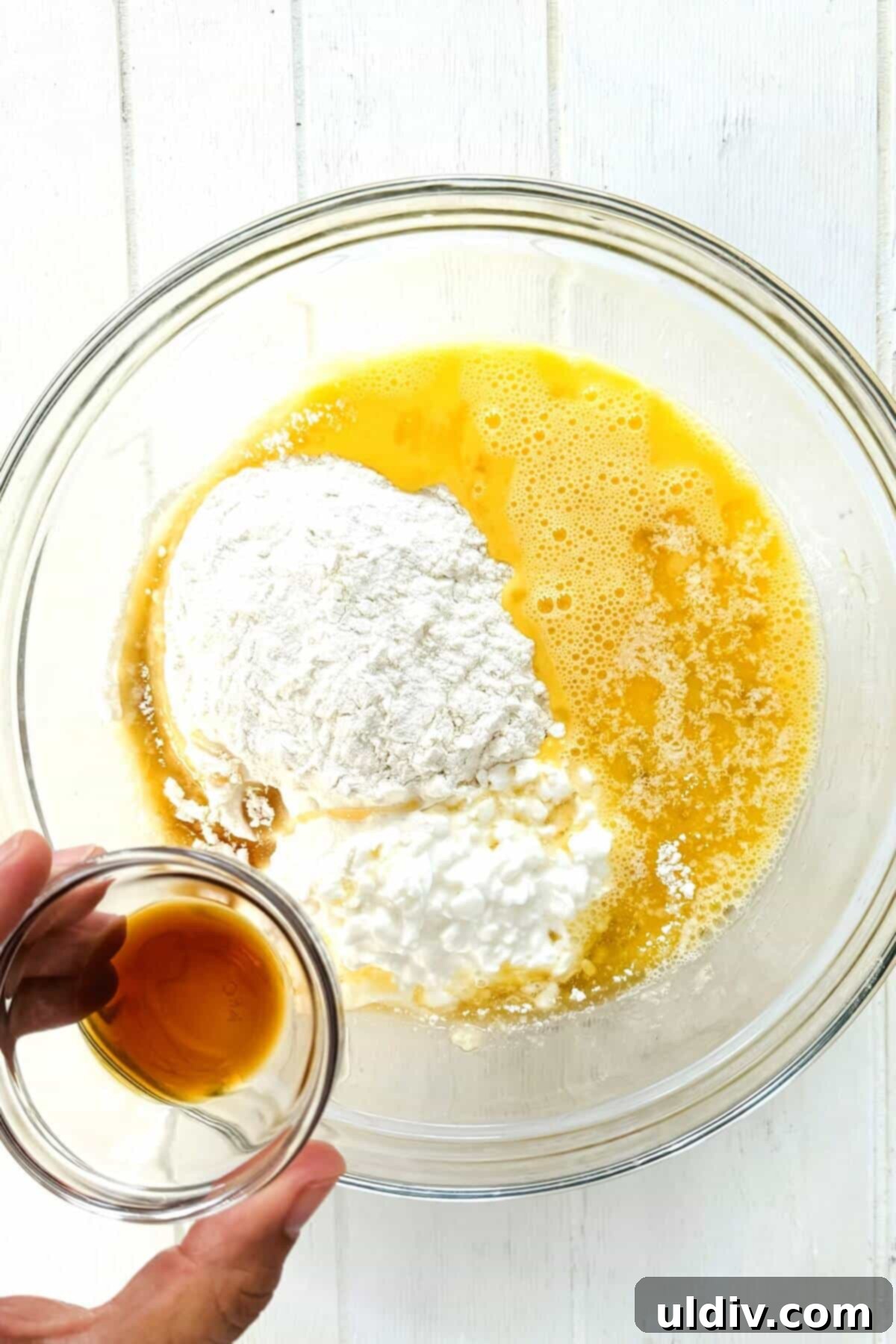 Power-Packed Banana Cottage Cheese Protein Pancakes 7 Pure vanilla extract being poured into the pancake batter ingredients in a glass bowl.
