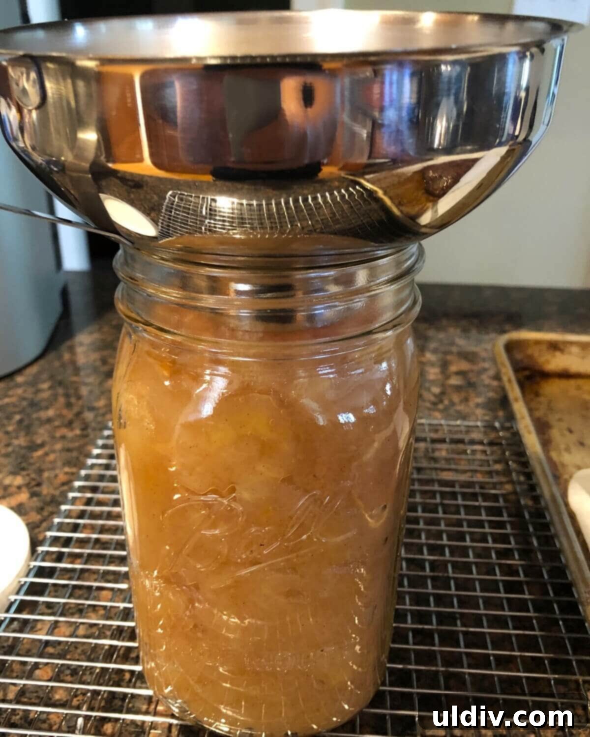 using a funnel to add applesauce to a jar.