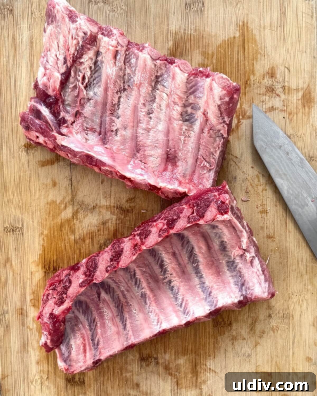 A rack of baby back ribs, already cut in half, with a section of the tough membrane being peeled off the underside.