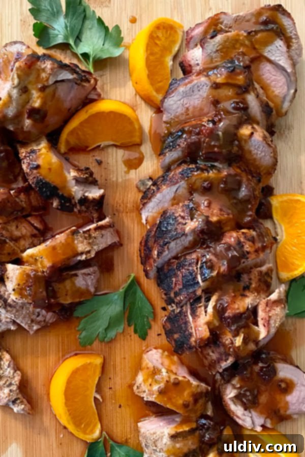 Close-up of perfectly grilled, sliced pork tenderloin, garnished with fresh orange wedges and a hint of sauce.