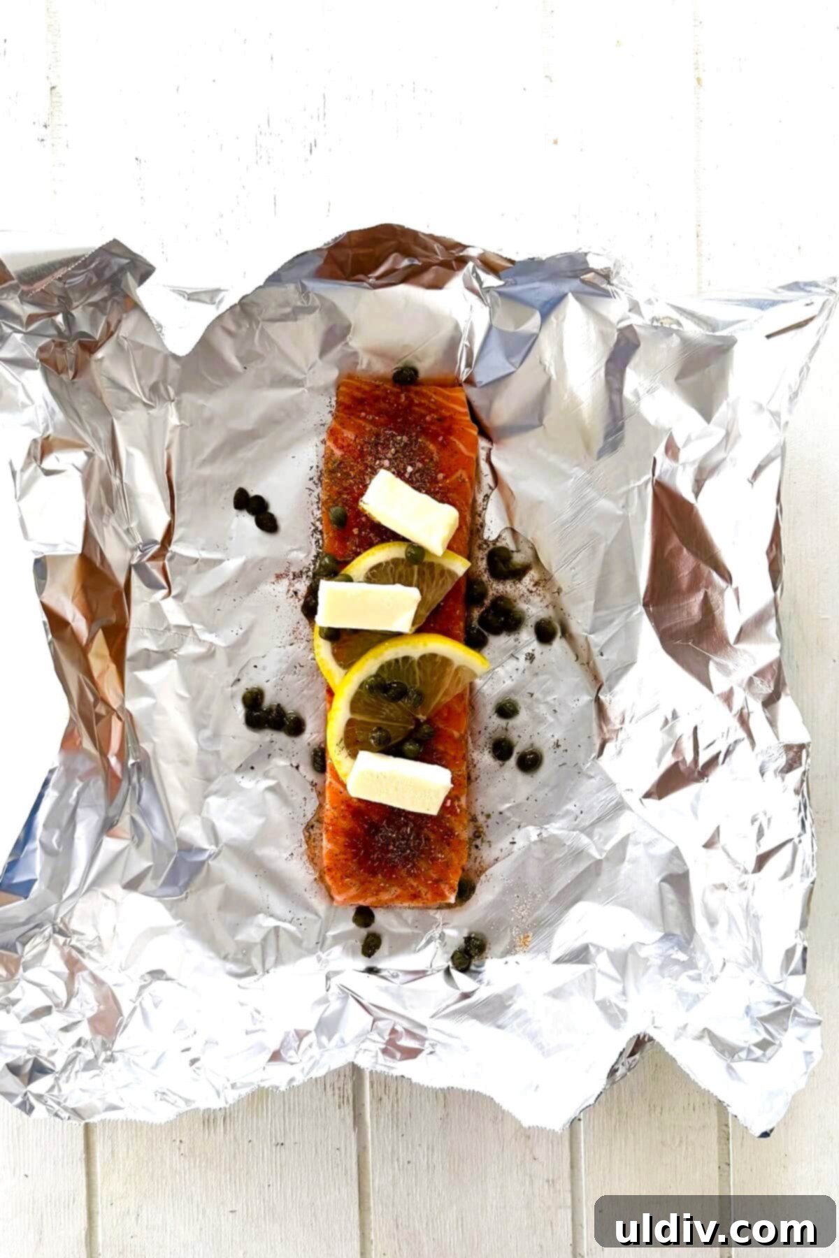 Simple Healthy Foil-Baked Salmon 5 An unbaked salmon fillet inside a foil packet, adorned with butter, lemon slices, and capers, ready for the oven.
