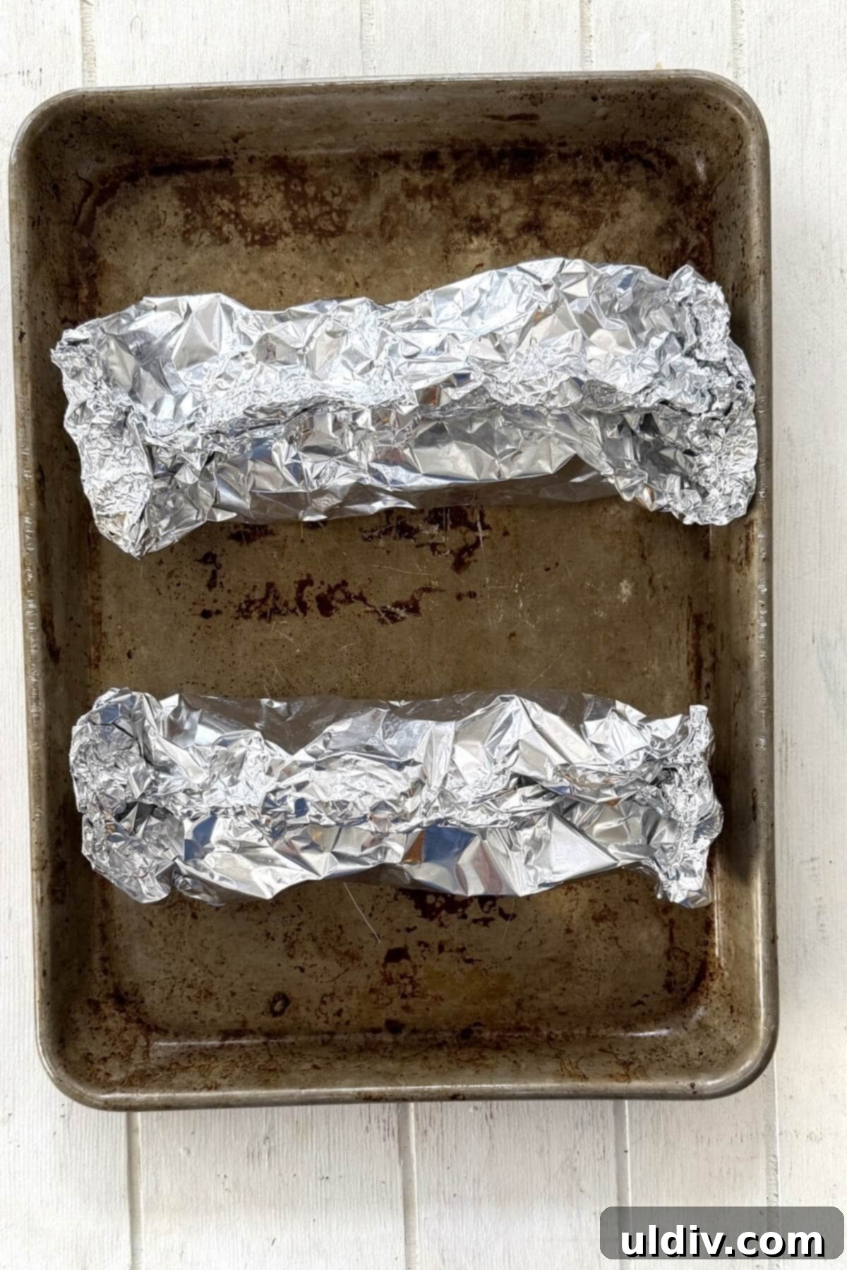 Simple Healthy Foil-Baked Salmon 6 Tightly sealed foil packets, each containing a seasoned salmon fillet, resting on a rimmed baking sheet.