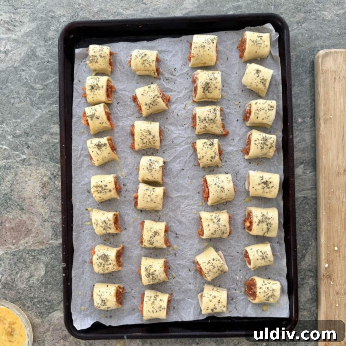 Homemade Pizza Sausage Rolls 10 Unbaked homemade sausage rolls, already sliced and arranged on a sheet pan.