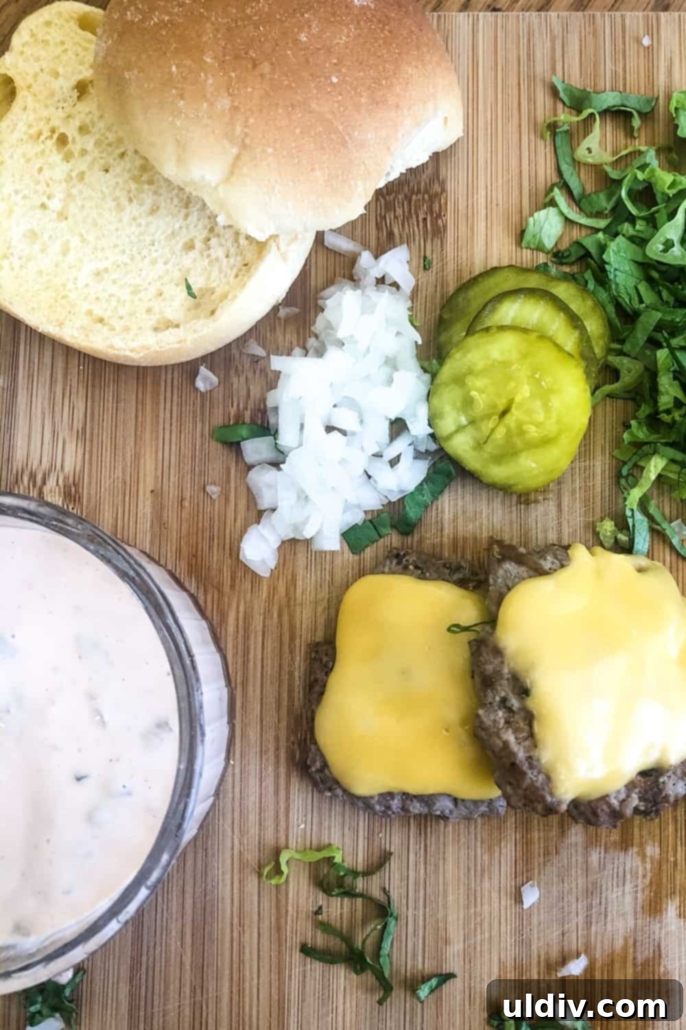 Copycat Big Mac Sliders 3 Assembled Big Mac slider components: bun halves, special sauce, pickle chips, chopped onion, cheeseburgers, and shredded lettuce.