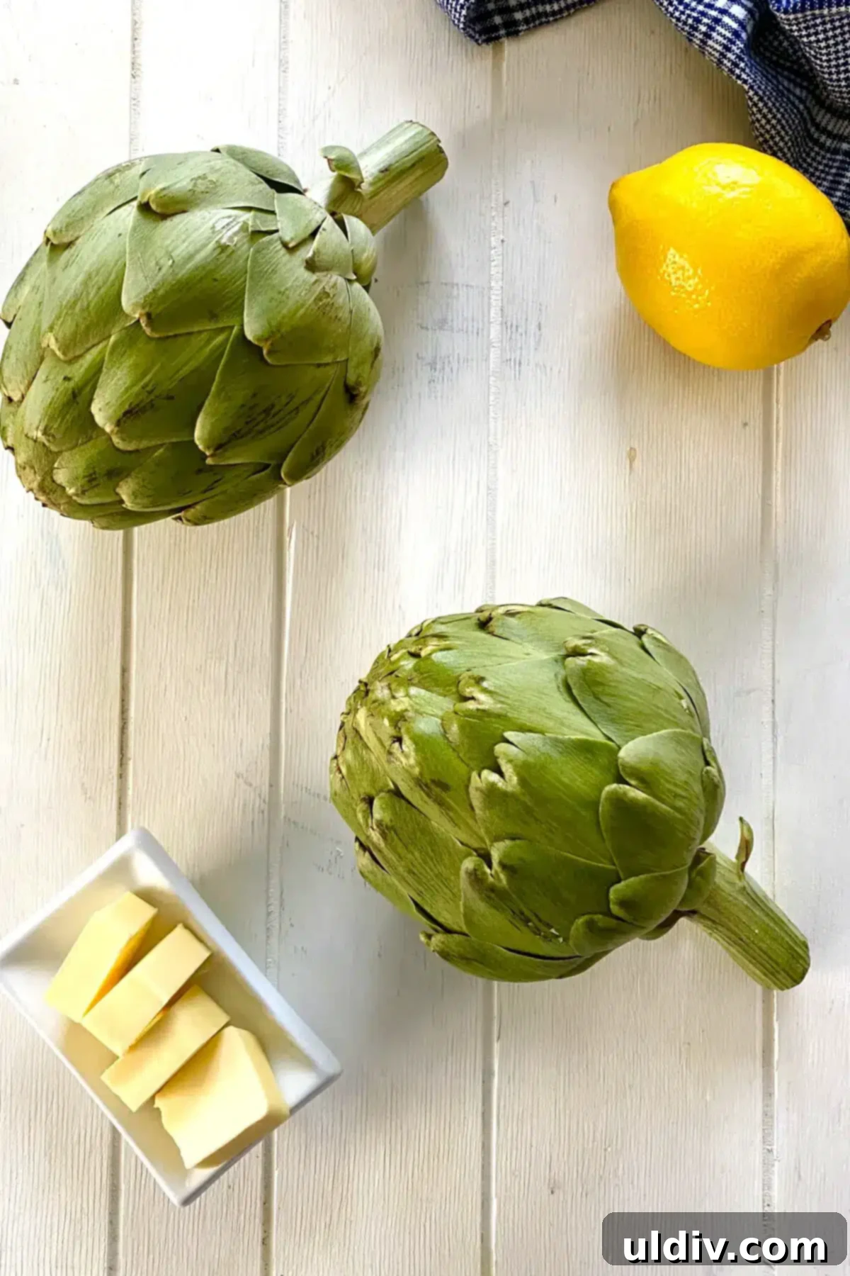 Quick & Easy Microwave Artichokes 4 A vibrant selection of two fresh artichokes, a stick of salted butter, and a bright lemon, set out as the essential ingredients for cooking.