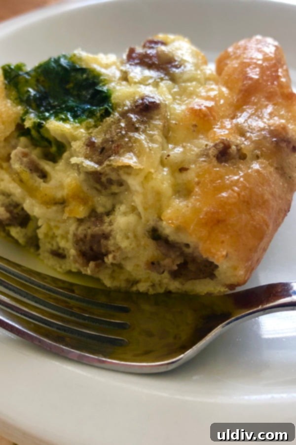 Effortless Sausage Spinach and Cheddar Breakfast Bake 6 A close-up of a single slice of homemade breakfast casserole, revealing layers of perfectly cooked egg, savory sausage, tender spinach, and melted cheddar cheese, highlighting its rich texture and appetizing appearance.