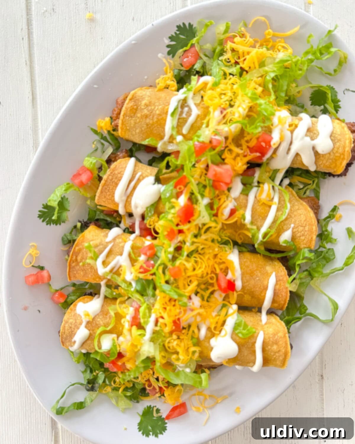 Crispy Baked Taquitos 11 A plate piled high with baked rolled tacos, garnished with fresh toppings like lettuce and tomatoes.
