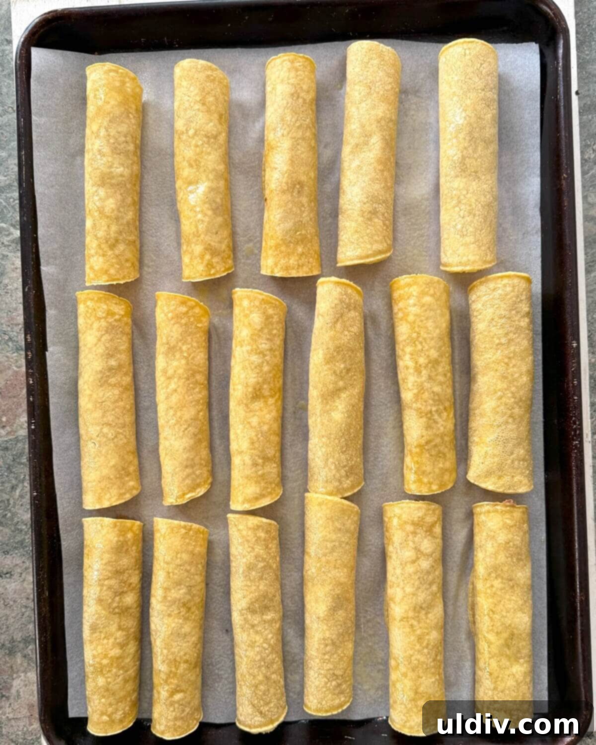 Crispy Baked Taquitos 9 Rolled taquitos arranged neatly, seam-side down, on a parchment paper-lined baking sheet.