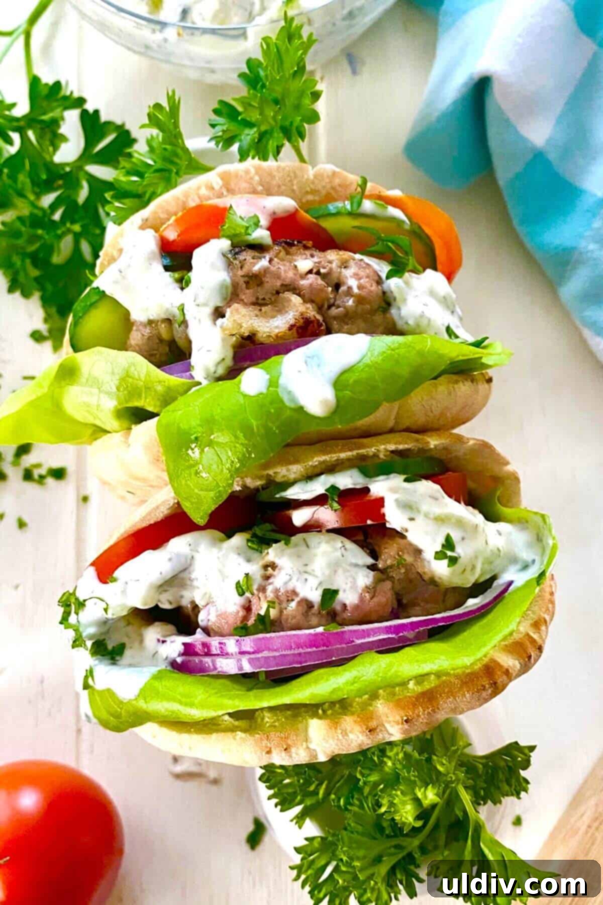 Two vibrant mini Greek turkey burgers nestled in pita bread, garnished with fresh vegetables and a dollop of tzatziki.
