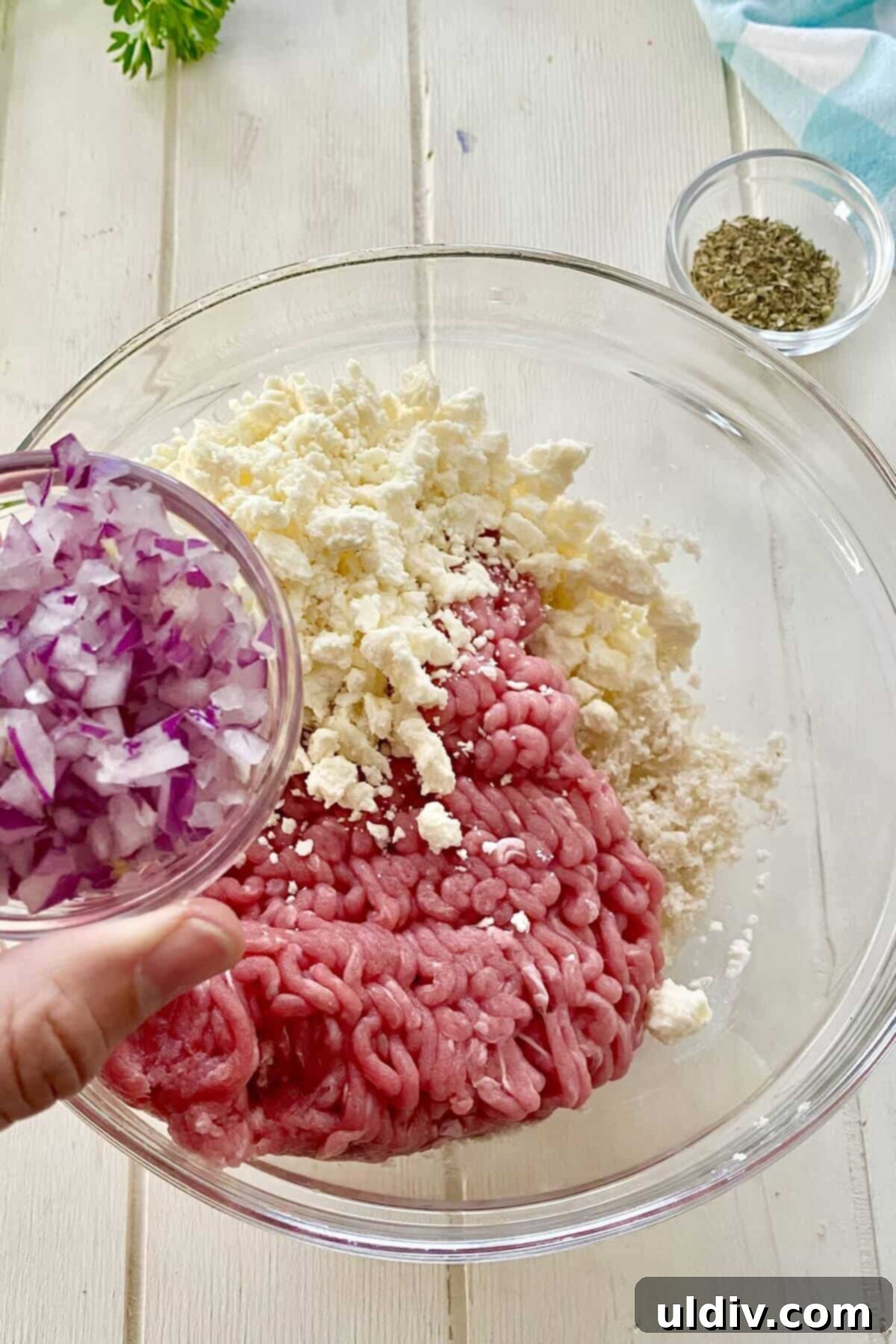 Adding finely chopped red onions to a bowl of ground turkey and crumbled feta cheese, ready for mixing.
