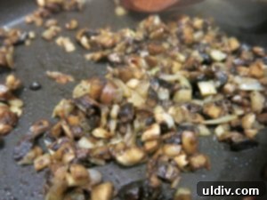 Chopped mushrooms sautéing in a pan until browned and liquid evaporated