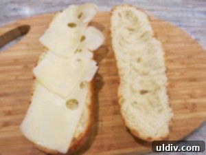 Sliced Swiss cheese laid on the bottom half of a baguette roll