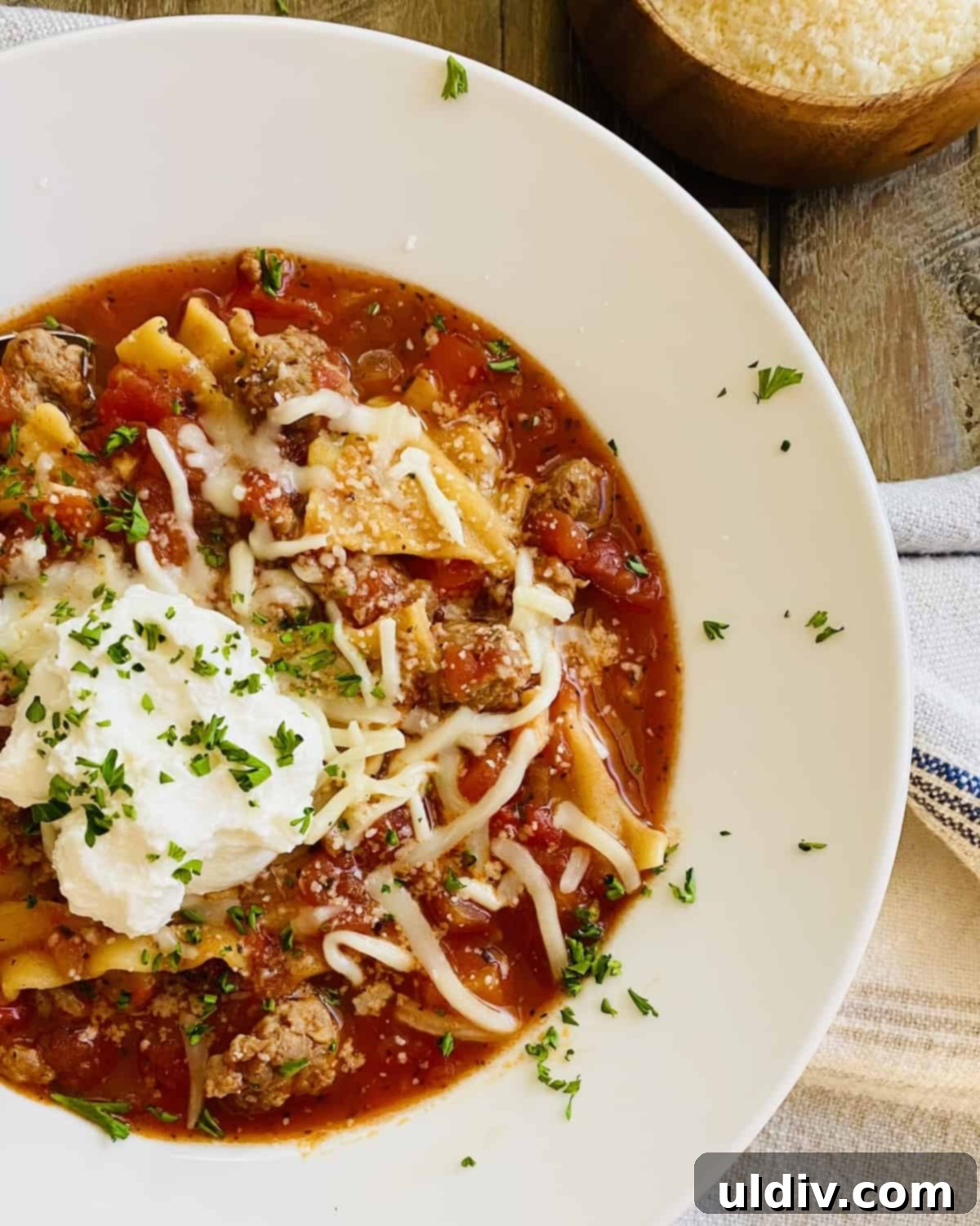 Easy One Pot Lasagna Soup 2 A white bowl of lasagna soup topped with ricotta cheese, fresh basil, and a sprinkle of Parmesan.
