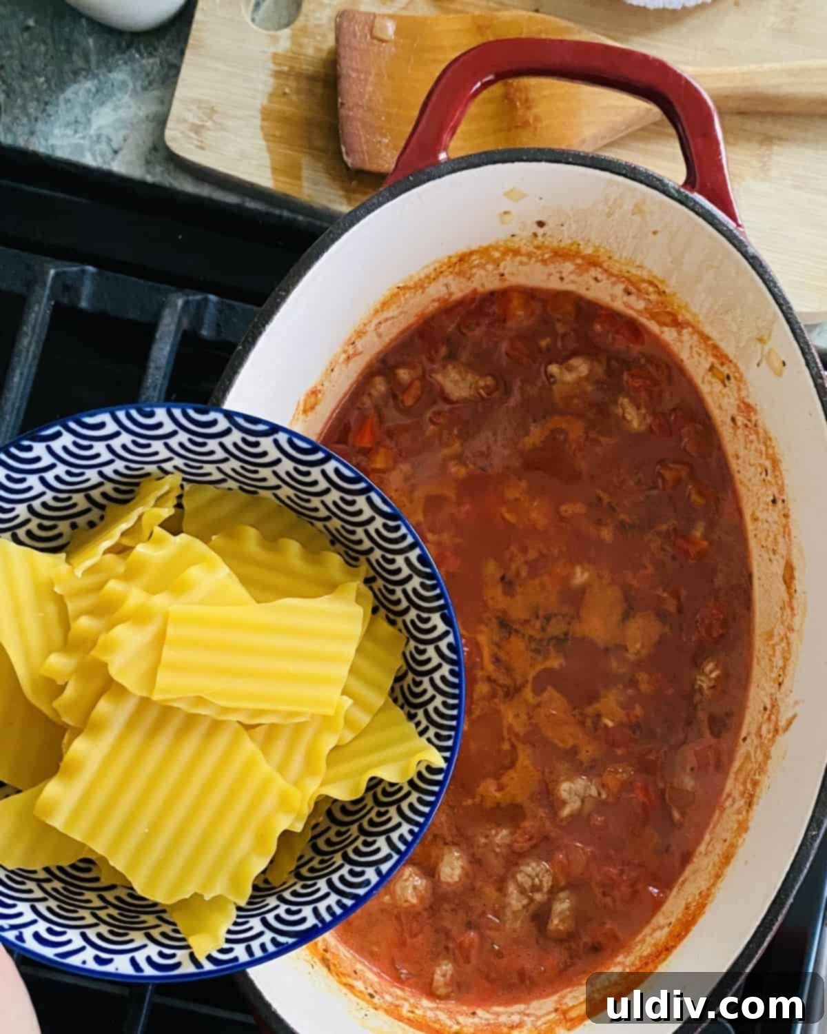 Adding broken lasagna noodles, kosher salt, and pepper to the simmering lasagna soup.